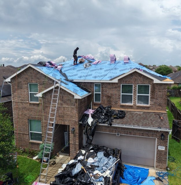 Roofer laying underlayment on the front slope of a two-story brick home during a replacement