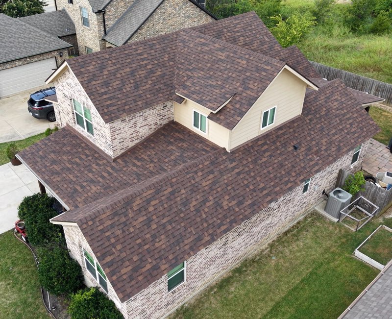 Aerial view of a completed brown architectural shingle roof on a brick home